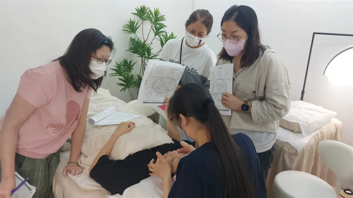 A bojin instructor demonstrating the method on her own face, holding a smooth-edged tool low against the jaw.
