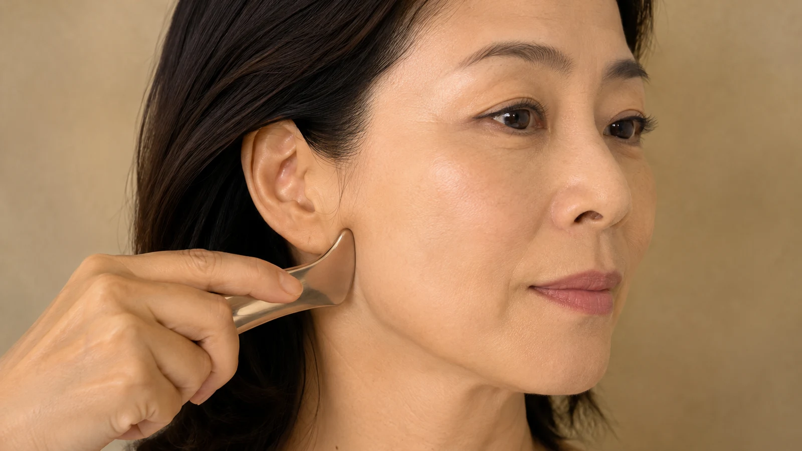 A mature woman working a bojin tool along the side of her jawline toward the ear