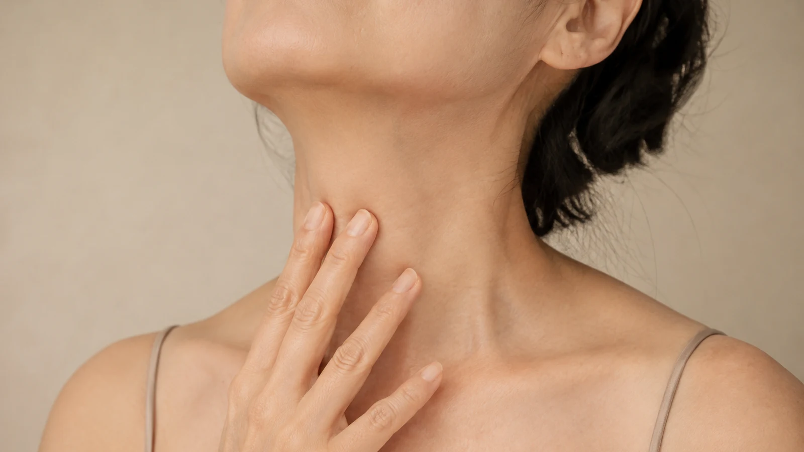 A mature woman with her chin lifted, fingertips resting gently on the front of her neck