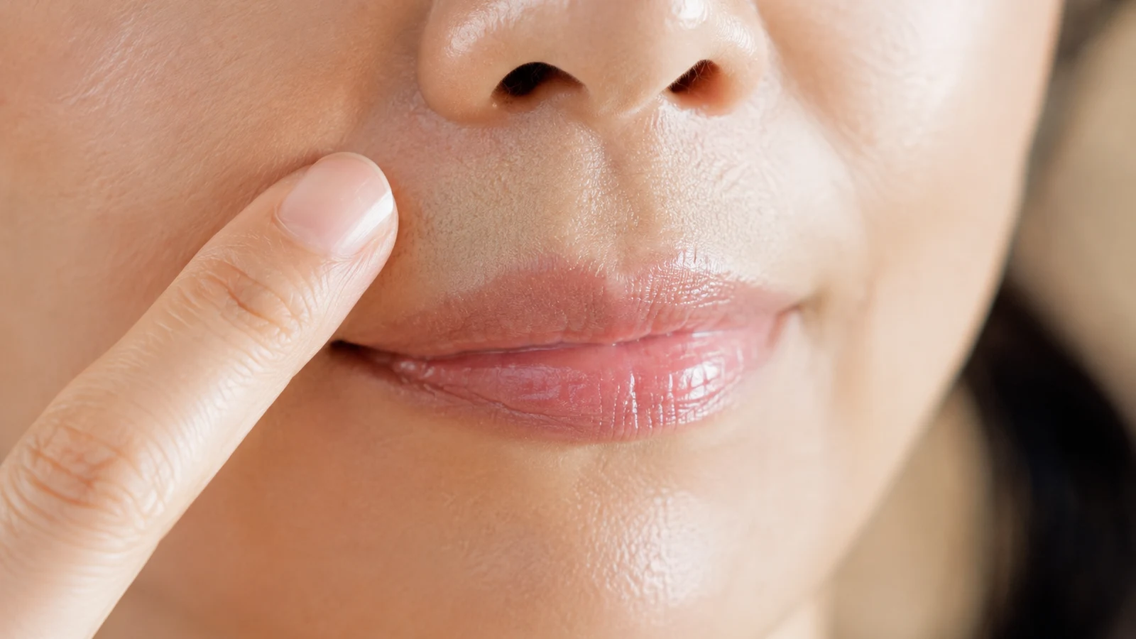A close-up of a fingertip gently smoothing the skin above the upper lip